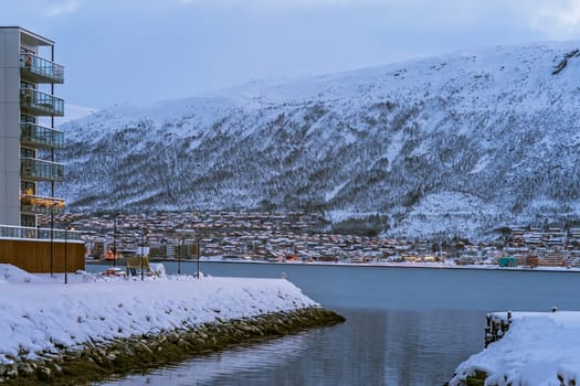 Residential hillside houses in Tromso suburb covered in a deep snow at dusk, Norway