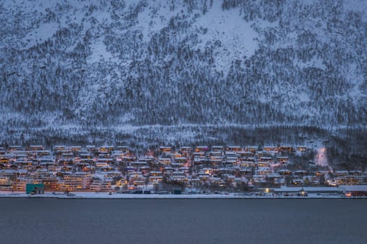Residential hillside houses in Tromso suburb covered in a deep snow at dusk, Norway