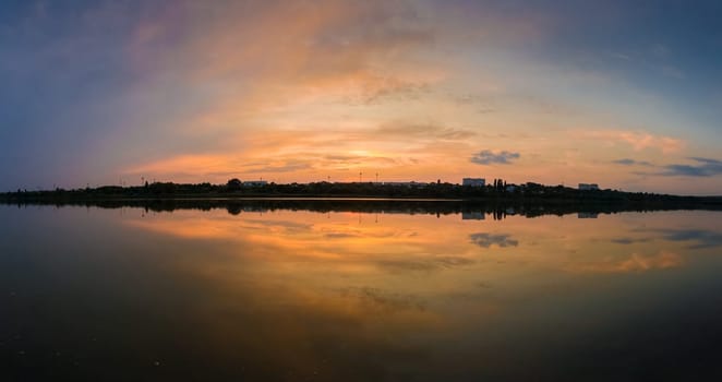 Panoramic view of colorful sunset clouds symmetric reflected on the lake surface. Idyllic summer evening, natural scene near a countryside pond with calm water.