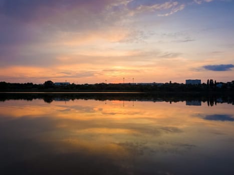 Colorful sunset clouds symmetric reflected on the lake surface. Idyllic summer evening, natural scene near a countryside pond with calm water.