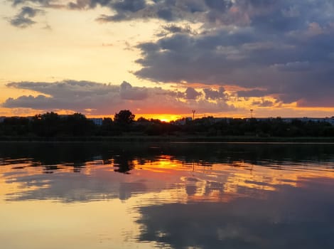 Beautiful sunset over the city horizon with reflection on the calm lake water in a silent summer evening...
