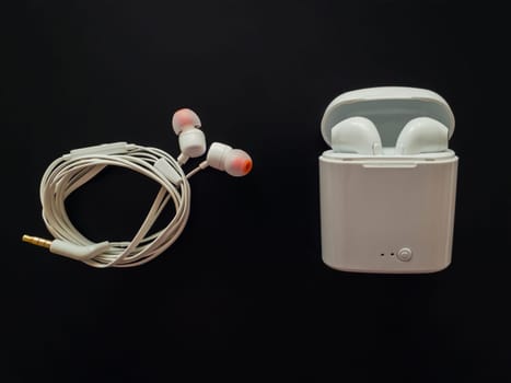 Comparison between classic wired headphones versus wireless earphones, air pods, isolated over black background. Pluses and minuses. Technology development tendencies, human conveniences concept.