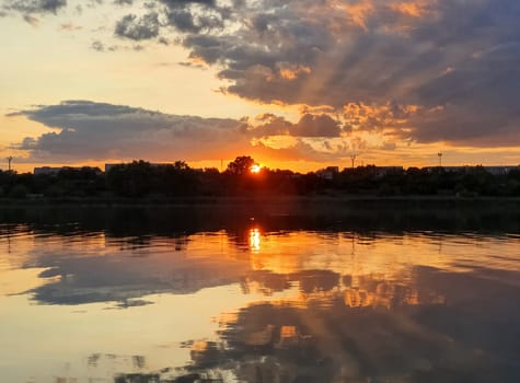 Wonderful sunset over the city horizon with reflection on the calm lake water in a silent summer evening..