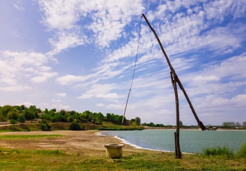 Idyllic countryside scene with an old water well sweep (shadoof) near the Delia lake (Moldova). Also called a counterpoise lift or well pole, is an ancient irrigation tool and used for watering crops.