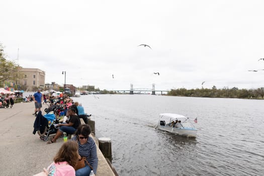Wilmington, North Carolina, USA - April 6, 2019: View of the Cape Fear River from the Riverfront park with people resting and eating during the The North Carolina.Azalea Festival