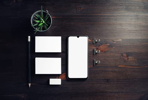 Cellphone and stationery on wooden background. Smartphone, business cards, pencil, eraser and plant. Flat lay.