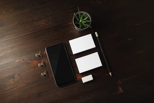 Blank stationery and smartphone on wood table background. Smartphone, business cards, pencil, eraser and plant.