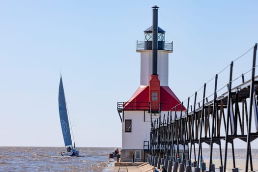 St. Joseph, Michigan, USA - May 4, 2019: View from the north pier, with the lighthouse and a sail boat leaving the harbor
