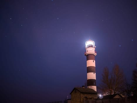 Black and white lighthouse at night in Baltic sea beach with stars