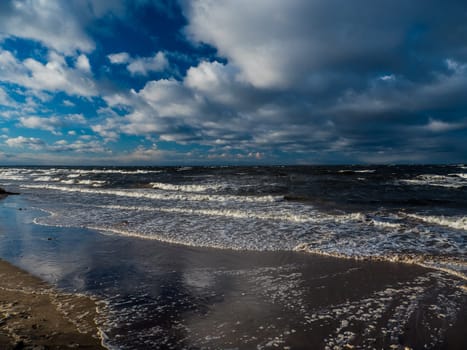 Baltic sea beach with blue cloudy sky and waves