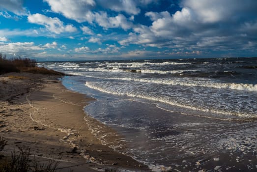 Baltic sea beach with blue cloudy sky and waves