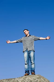 young casual man on top of a rock with the sky as background