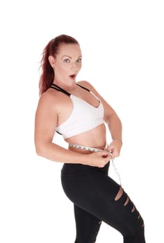 A pretty woman standing in workout outfits measuring her stomach.and is very surprised what she sees, isolated for white background.