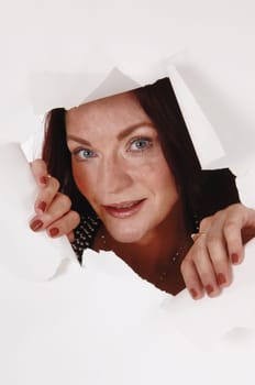 A close up image of a pretty woman peeking through a hole in a paper.opening it with her hands, isolated for white background.