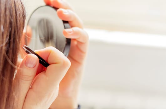 Female person using tweezers and a mirror with natural light. Personal care and beauty. Makeup accessories