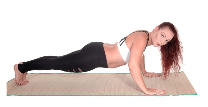 A middle age woman in sports outfit doing push ups on a mads.with her red hair and nice figure, isolated for white background.