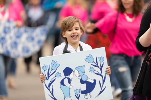 Holland, Michigan, USA - May 11, 2019: Tulip Time Parade, Woman accompanying children displaying their dutch related artworks during the parade