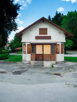 Frontal view of an old small station kiosk closed with boards and wooden panels in a rural Bavarian environment with trees and blue sky.