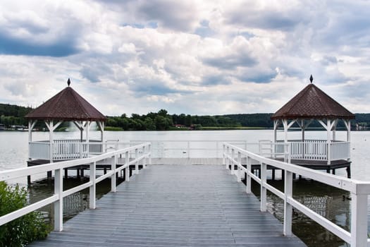 Beautiful white roofed pier with wooden huts on lake, green forest and puffy clouds in background, Barlinek, Poland