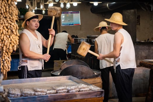 Xian, China -  July 2019 : Two men hitting hard with big wooden hammers to crack grain which will be used in making of sweet snack for sale on the street, Muslim Quarter
