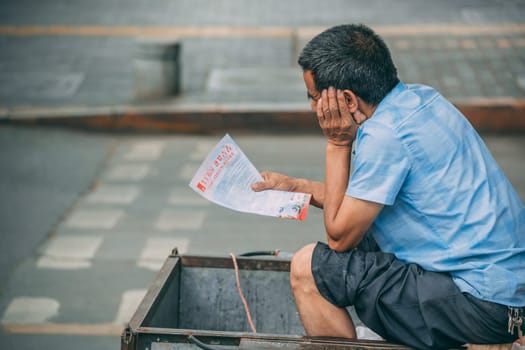 Xian, China -  July 2019 : Chinese man reading information advertising leaflet while sitting inside a wheeled trolley
