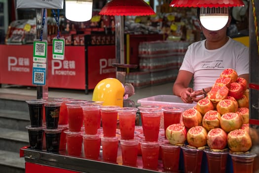 Xian, China -  July 2019 : Man selling plastic cup filled with freshly squeezed pomegranate juice in a stall in Muslim Quarter in Xian town, Shaanxi Province