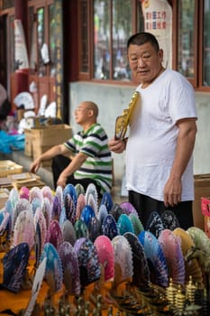 Xian, China -  July 2019 : Older man selling colorful paper fans on a hot day on the street in the Muslim Quarter