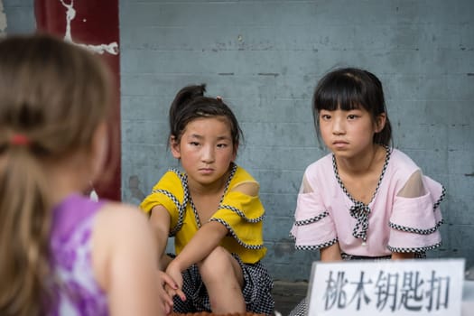 Xian, China -  July 2019 : Two little Chinese girls looking at a Caucasian girl standing in front of a souvenir stand on the street in the Muslim Quarter