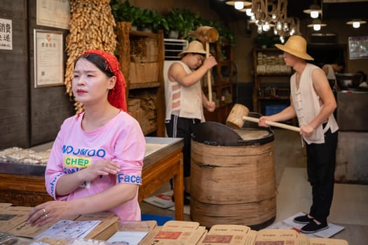 Xian, China -  July 2019 : Two men hitting hard with big wooden hammers to crack grain which will be used in making of sweet snack for sale on the street, Muslim Quarter