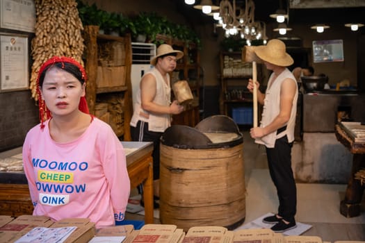 Xian, China -  July 2019 : Two men hitting hard with big wooden hammers to crack grain which will be used in making of sweet snack for sale on the street, Muslim Quarter