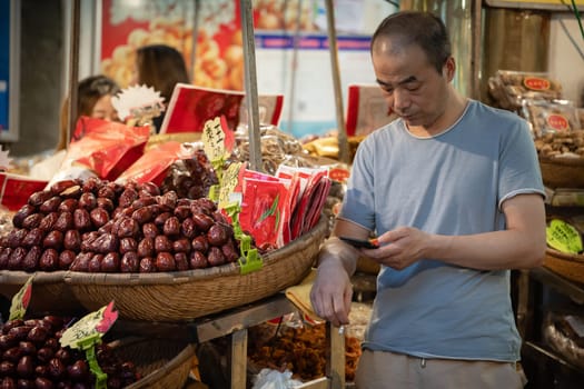Xian, China -  July 2019 : Bored fruit seller checking his smartphone on a stall in Muslim Quarter