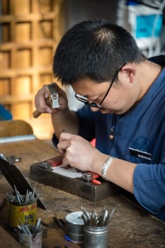 Xian, China -  July 2019 : Man using hammer to repair broken jewellery on the street market in the Muslim Quarter, Xian town, Shaanxi Province