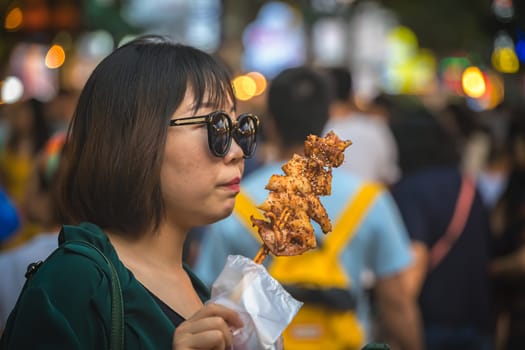Xian, China -  July 2019 : Portrait of a Chinese woman with a big black sunglasses eating snack from a stick on the street in the Muslim Quarter