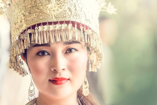 Zhangjiajie, China -  August 2019 : Cultural portrait of a beautiful chinese woman in a traditional chinese dress, wearing a golden decorated hat and standing outdoor