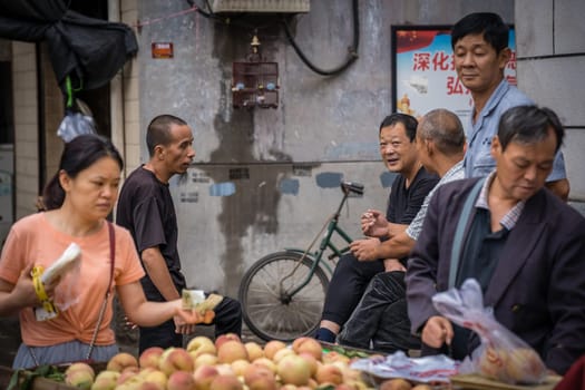 Xian, China -  July 2019 : Group of male friends talking and chatting behind a fruit stall in Muslim Quarter in Xian town, Shaanxi Province