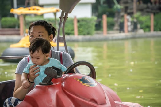 Xian, China -  July 2019 : Mother and child in a fun boat on a small lake in Childrens Park in Xian town