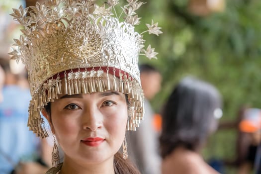 Zhangjiajie, China -  August 2019 : Cultural portrait of a beautiful chinese woman in a traditional chinese dress, wearing a golden decorated hat and standing outdoor