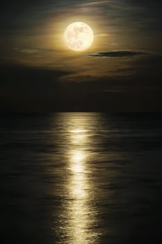 Super full moon and cloud in the yellow sky above the ocean horizon at midnight, moonlight reflect the water surface and wave, Beautiful nature landscape view at night scene of the sea for background