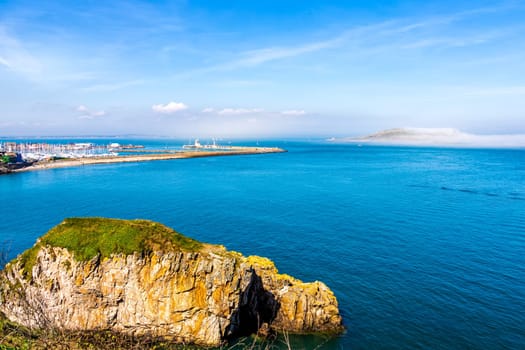 Low lying fog or mist approaching and covering Irelands Eye island, unusual phenomenon, panoramic view from Howth view point on harbour Dublin Ireland