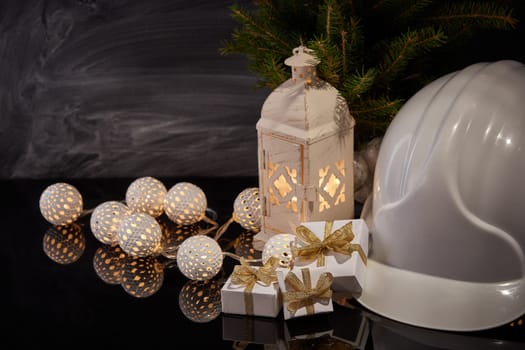 Construction hard hat, candle lantern, gift boxes and Christmas ornament on black background. Construction New Year, Christmas background with copy space. For greeting card or advertising