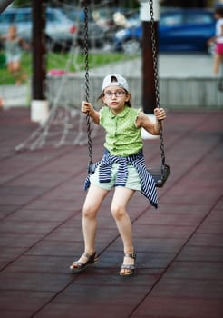 Child girl is swinging on a swing on the playground. Selective focus.
