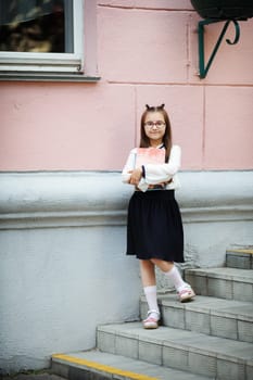 Schoolgirl in school uniform with textbooks in her hands. Child girl stands on the steps of the school. Vertical shot. Selective focus.
