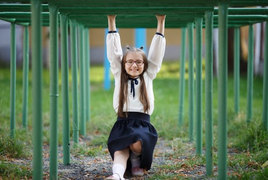 Cheerful child girl hanging on the horizontal bar. Schoolgirl is having fun on the playground. Selective focus.