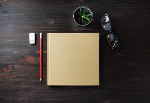 Blank book and stationery on wooden background. Notepad, glasses, pencil, eraser and plant. Flat lay.