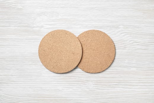 Two blank cork beer coasters on light wooden background. Responsive design template. Flat lay.
