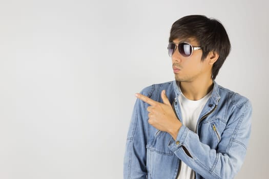 Young Asian Man in Jeans Jacket or Denim Jacket Wear Sunglasses and Pointing Finger. Denim or Jeans Jacket Men Fashion on Gray Background