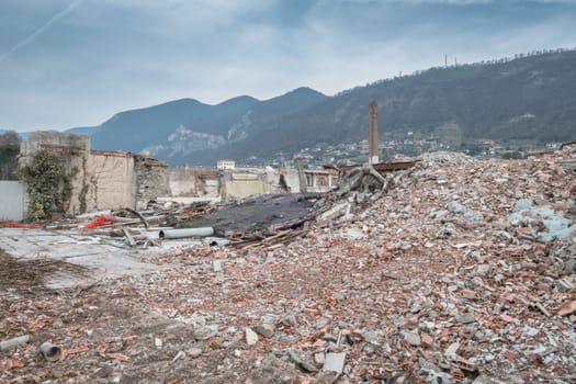 Demolition of buildings in urban environments. On background green mountains and a cloudy sky.