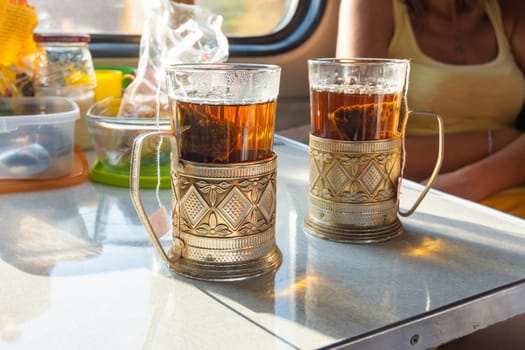 On the table in the train compartment are glasses with tea in metal cup holders.