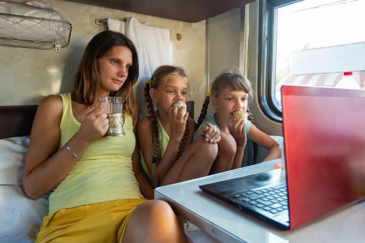Mom drinks tea, children eat ice cream on a train, look at a laptop together