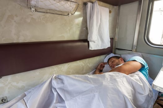 A man sleeps on the bottom shelf in a train car